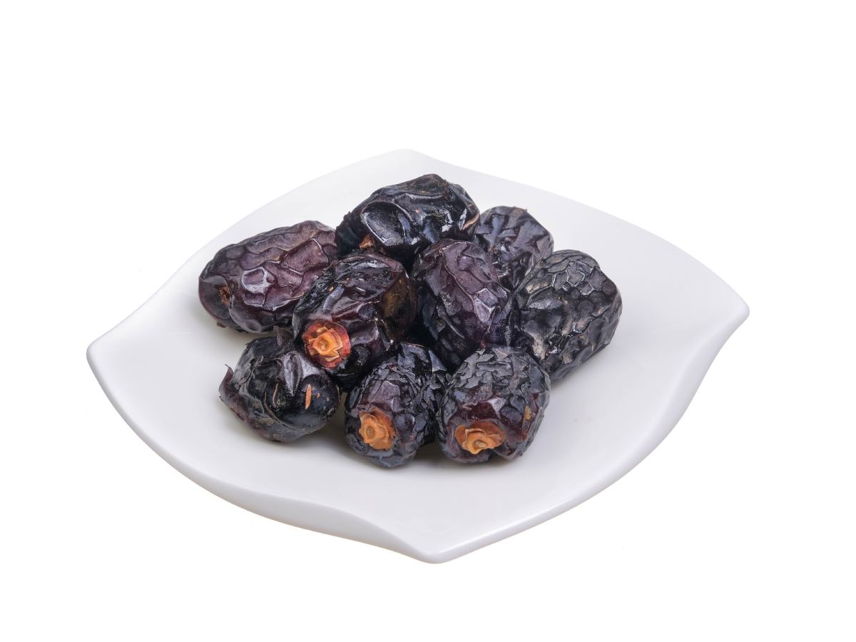 Ajwa dates displayed in elegant pink ceramic bowls on a neutral background, with white floral decor—emphasizing their spiritual significance and deep black, wrinkled texture.