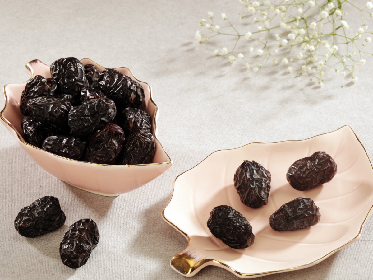 Ajwa dates displayed in elegant pink ceramic bowls on a neutral background, with white floral decor—emphasizing their spiritual significance and deep black, wrinkled texture.